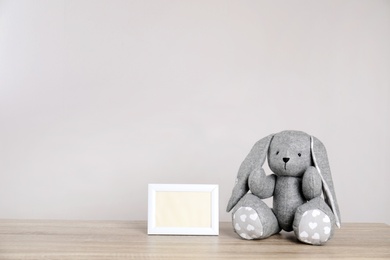 Photo of Photo frame with space for text and adorable toy bunny on table against light background. Child room elements