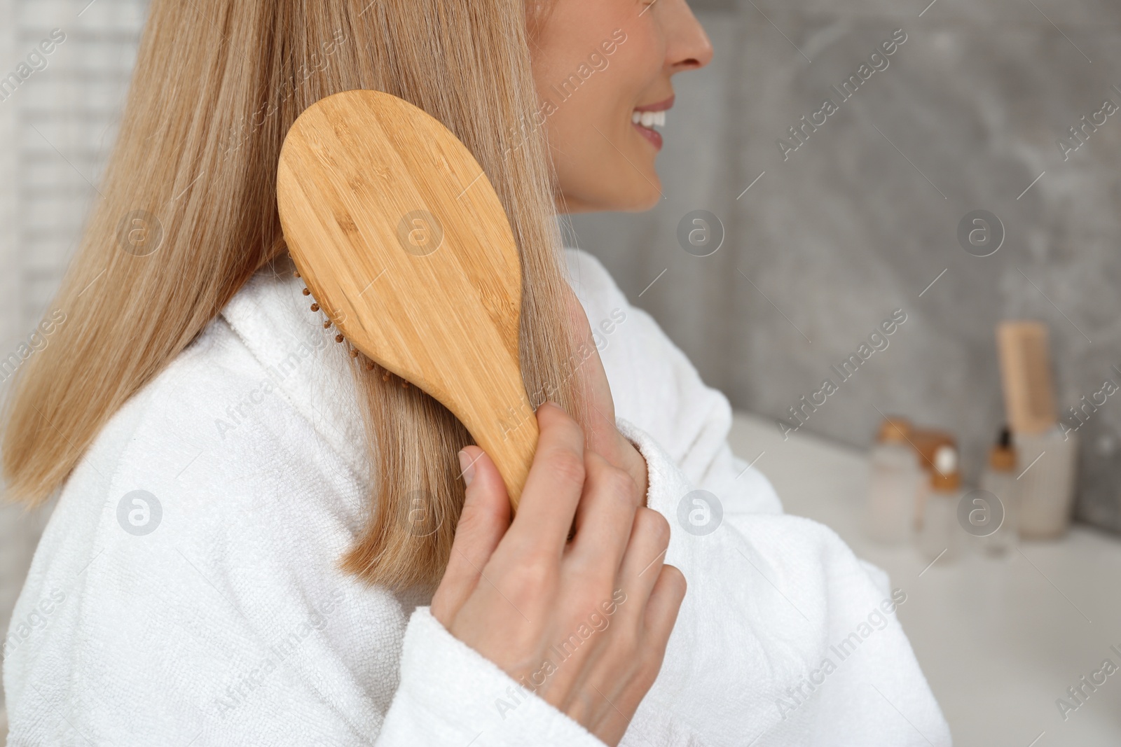 Photo of Woman in white robe brushing her hair indoors, closeup