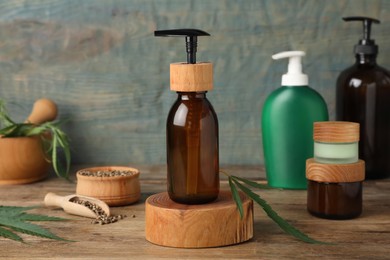 Different hemp cosmetics and green leaves on wooden table