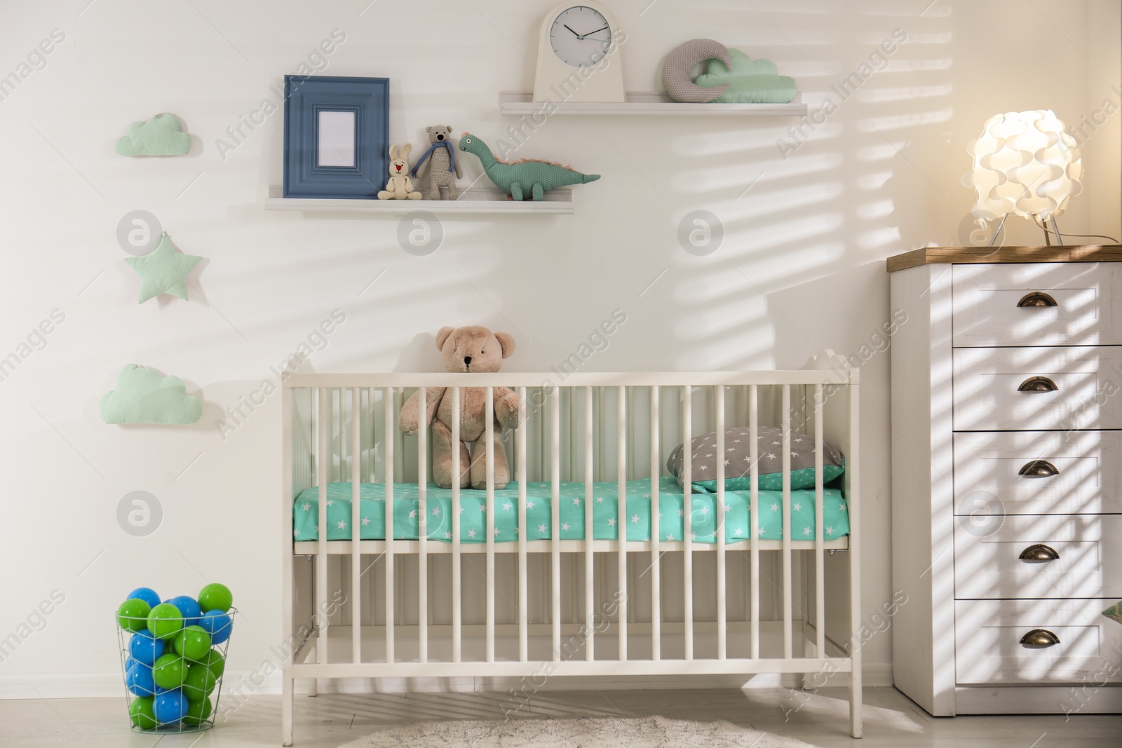 Photo of Cute nursery interior with comfortable crib near white wall