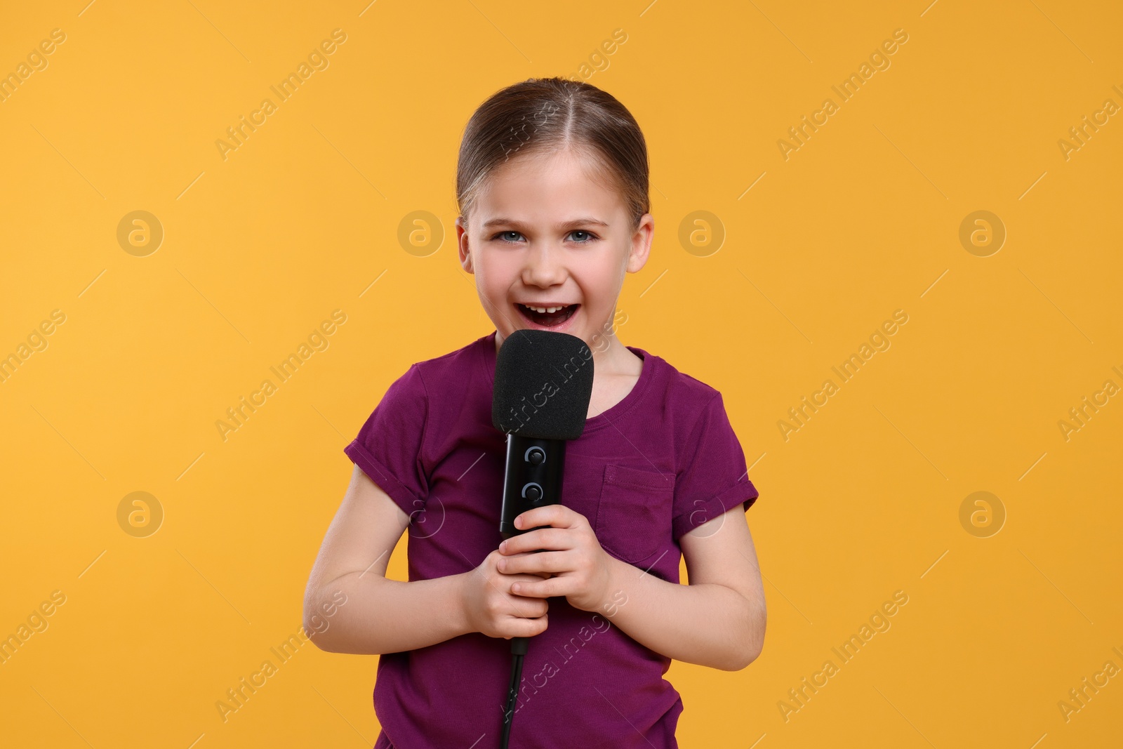 Photo of Cute little girl with microphone singing on yellow background