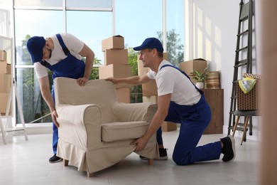 Moving service employees carrying armchair in room