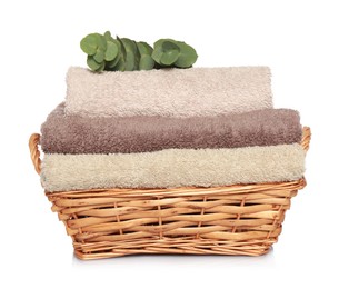 Wicker basket with folded soft terry towels and eucalyptus branch on white background