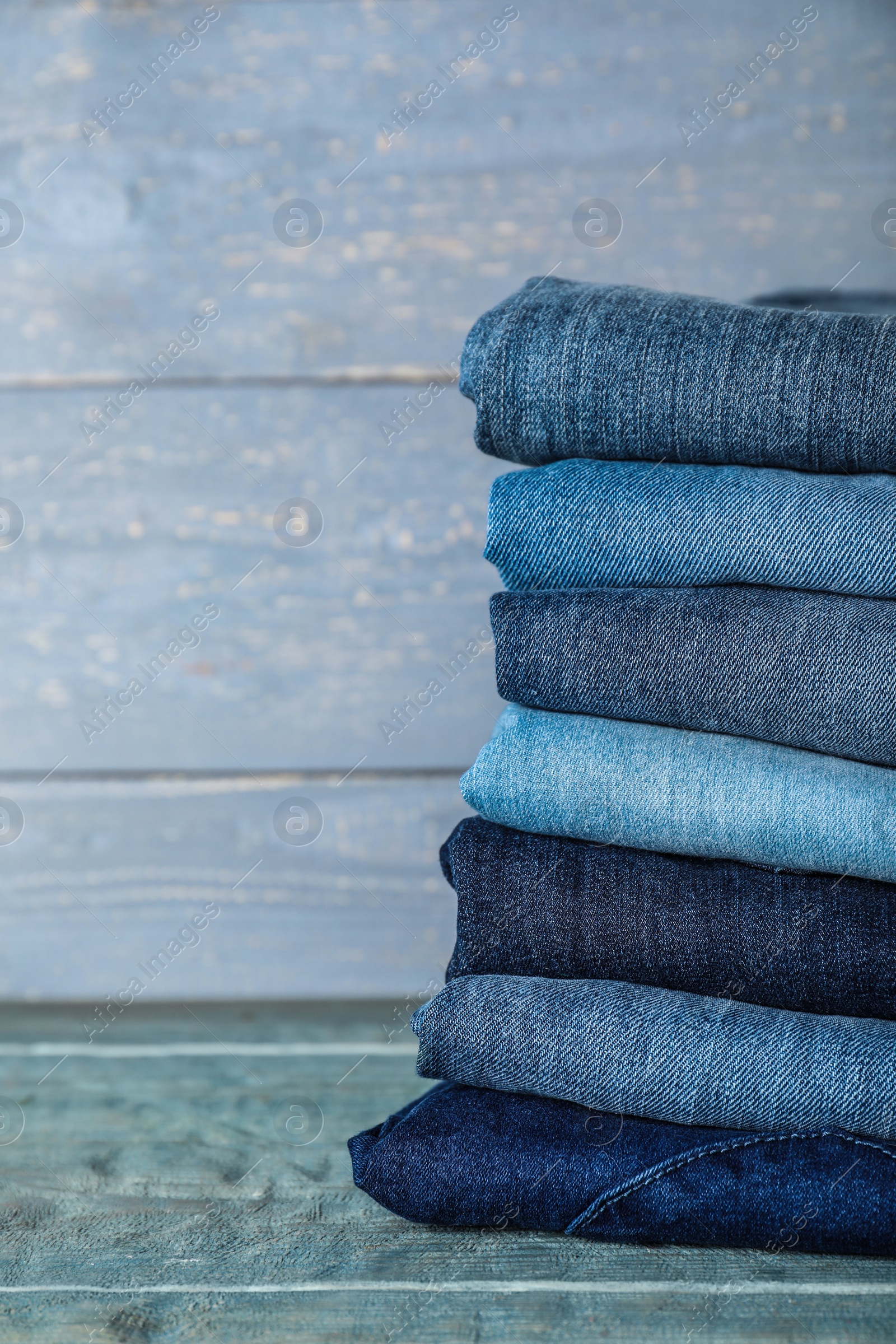 Photo of Stack of different jeans on blue wooden table. Space for text