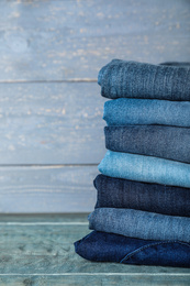 Photo of Stack of different jeans on blue wooden table. Space for text