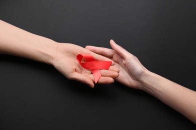 Photo of Women holding red awareness ribbon on black background, top view. World AIDS disease day