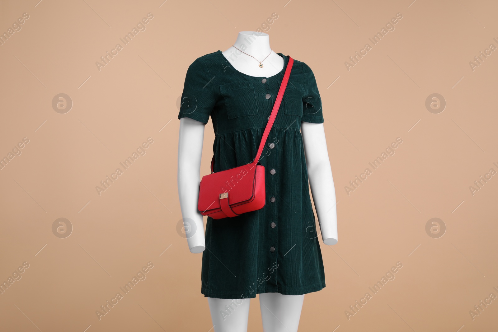 Photo of Female mannequin with necklace and bag dressed in stylish dark green dress on beige background