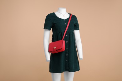 Photo of Female mannequin with necklace and bag dressed in stylish dark green dress on beige background