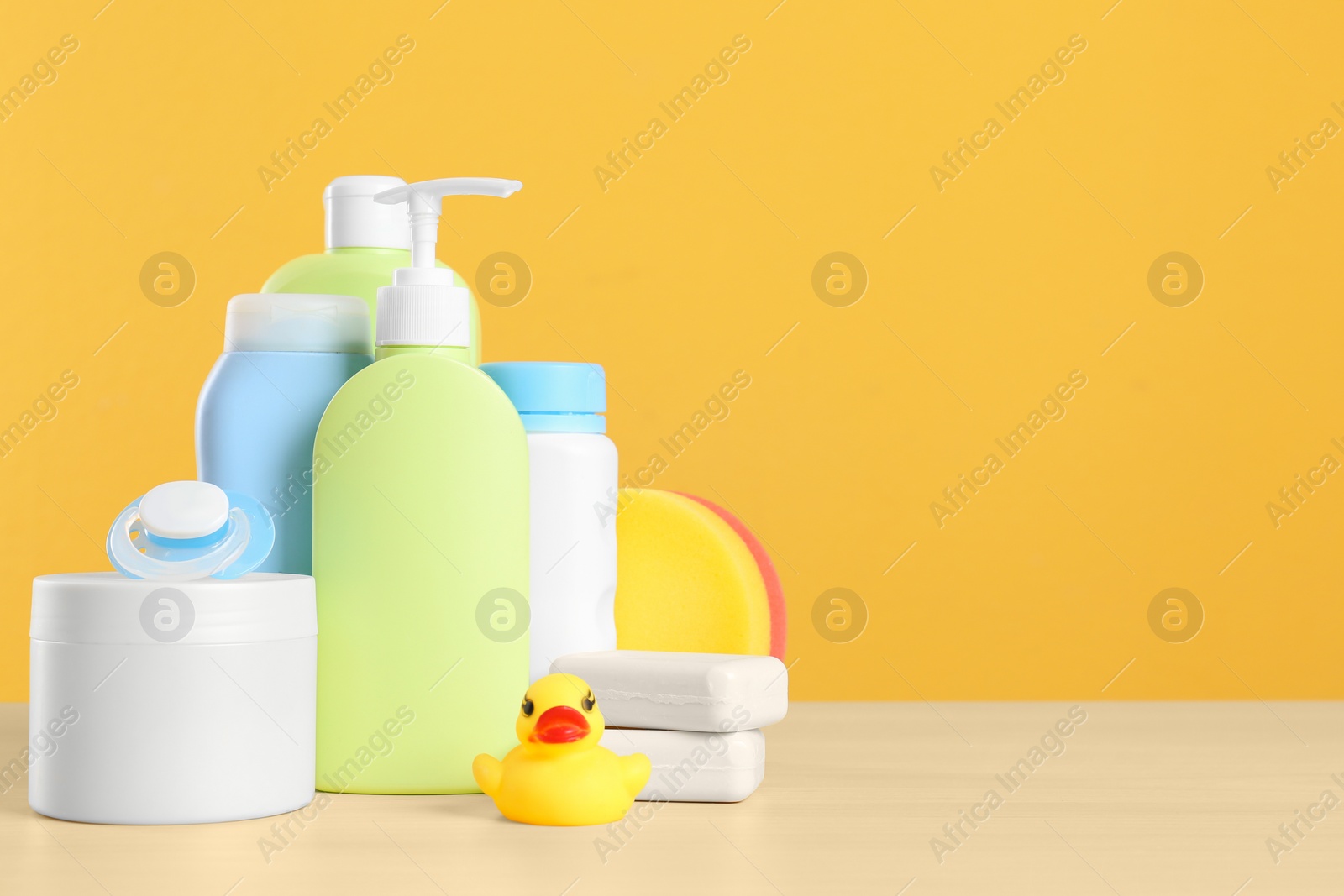 Photo of Baby cosmetic products, toy and pacifier on table against color background. Space for text