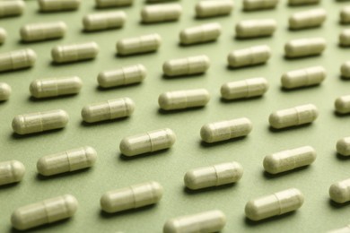 Many vitamin capsules on olive background, closeup