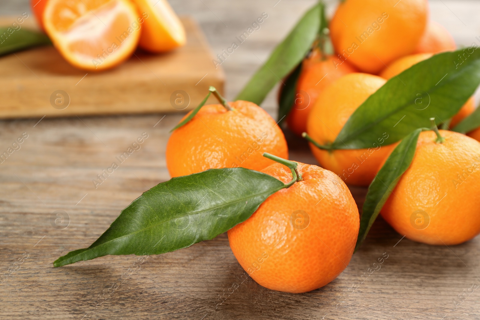 Photo of Fresh ripe tangerines with green leaves on wooden table, closeup