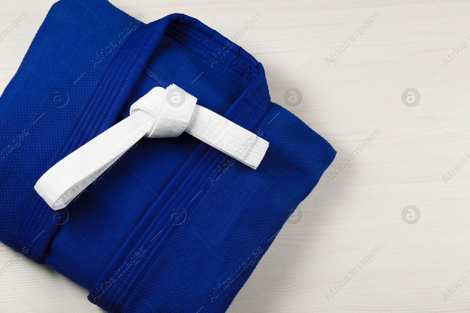 Photo of White karate belt and blue kimono on wooden background, top view. Space for text