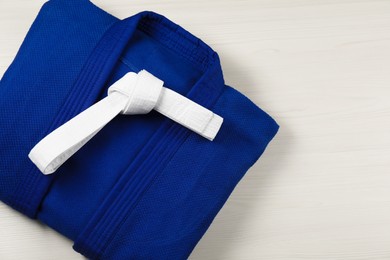 White karate belt and blue kimono on wooden background, top view. Space for text