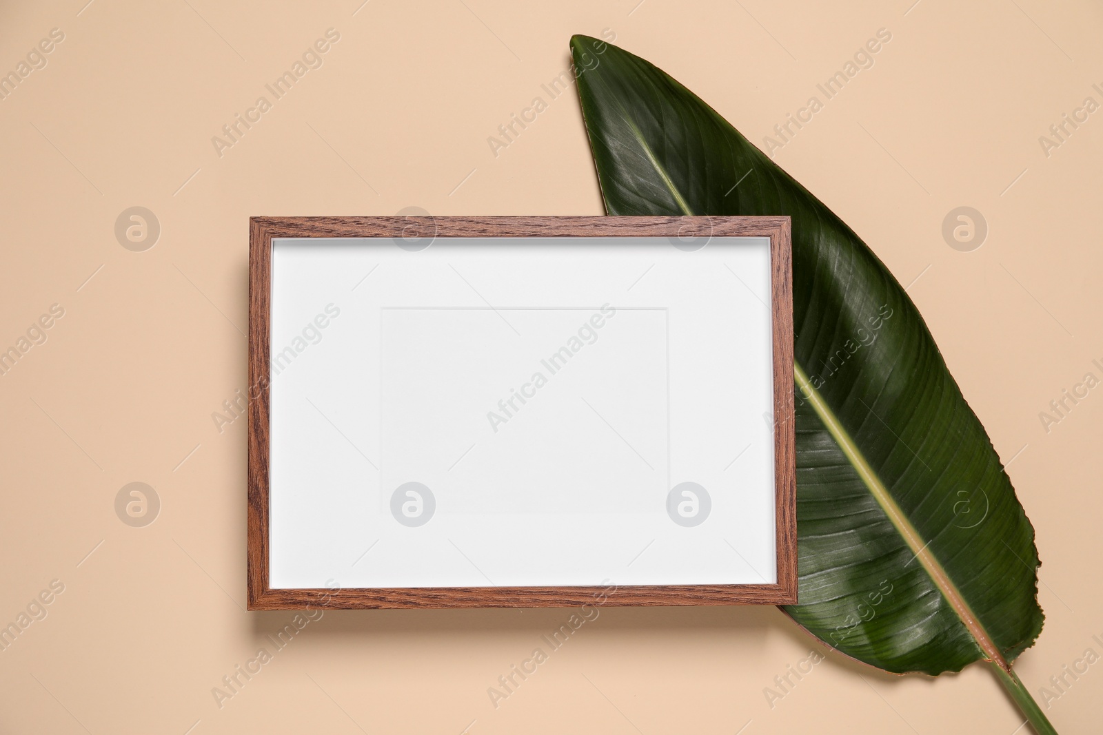 Photo of Empty photo frame and green leaf on beige background, flat lay. Space for design