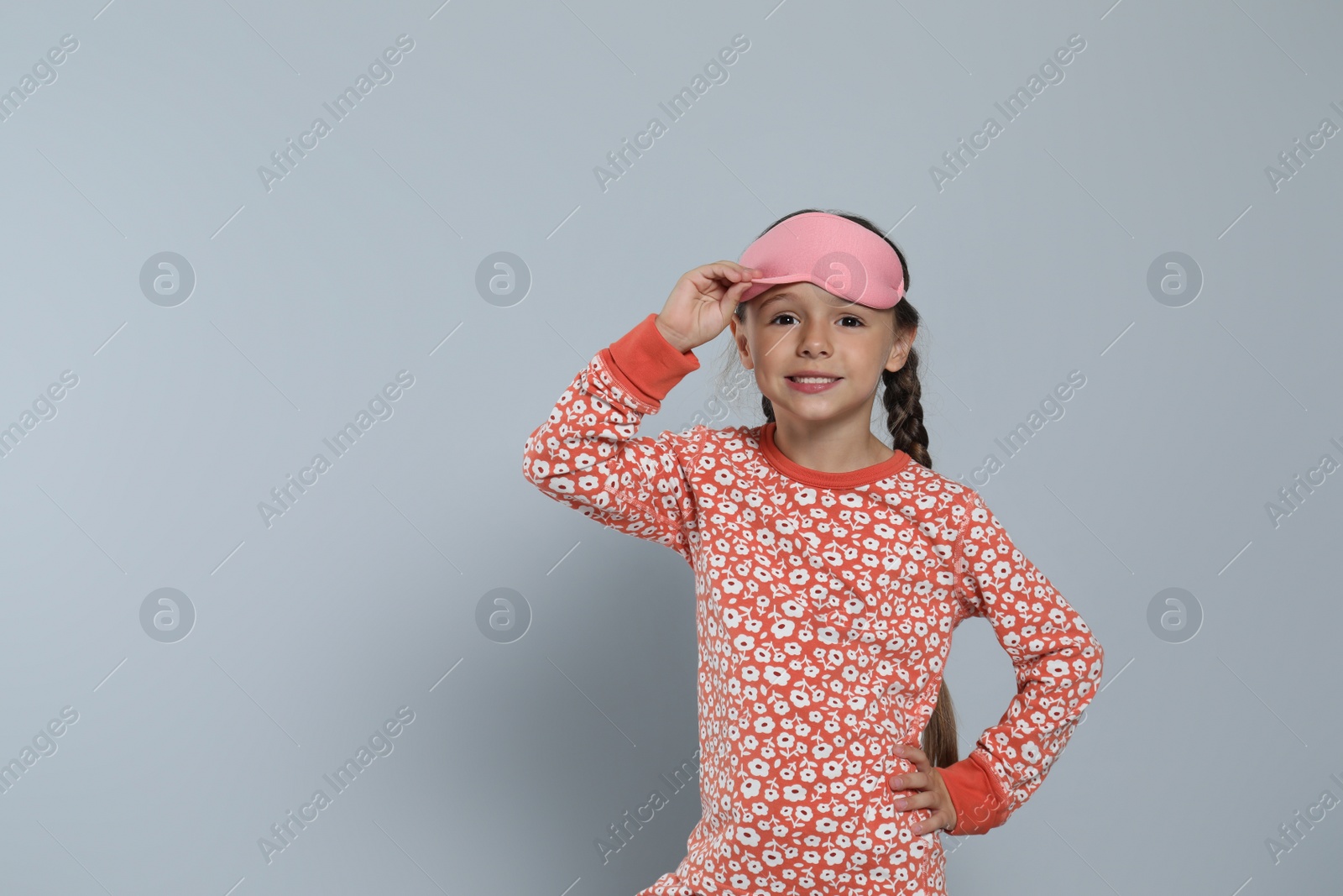 Photo of Cute girl in pajamas with pink sleep mask on light grey background. Space for text