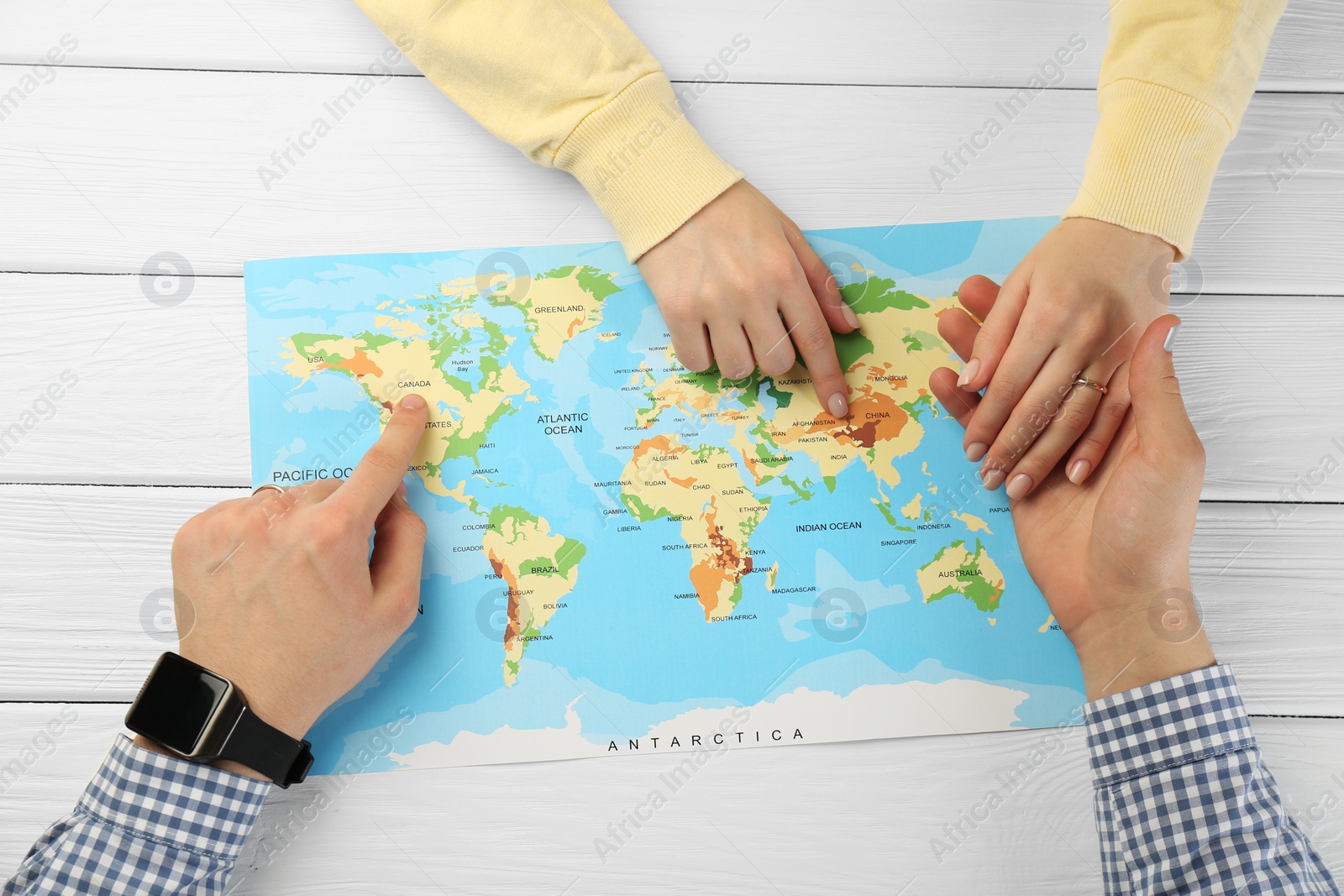 Photo of Man and woman planning their honeymoon trip with world map at white wooden table, top view