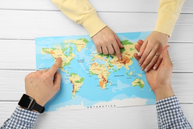 Man and woman planning their honeymoon trip with world map at white wooden table, top view