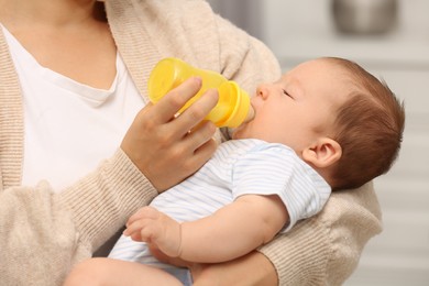 Mother feeding her cute child with infant formula indoors