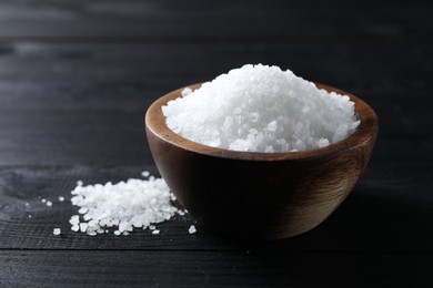 Photo of Organic salt in bowl on black wooden table, closeup