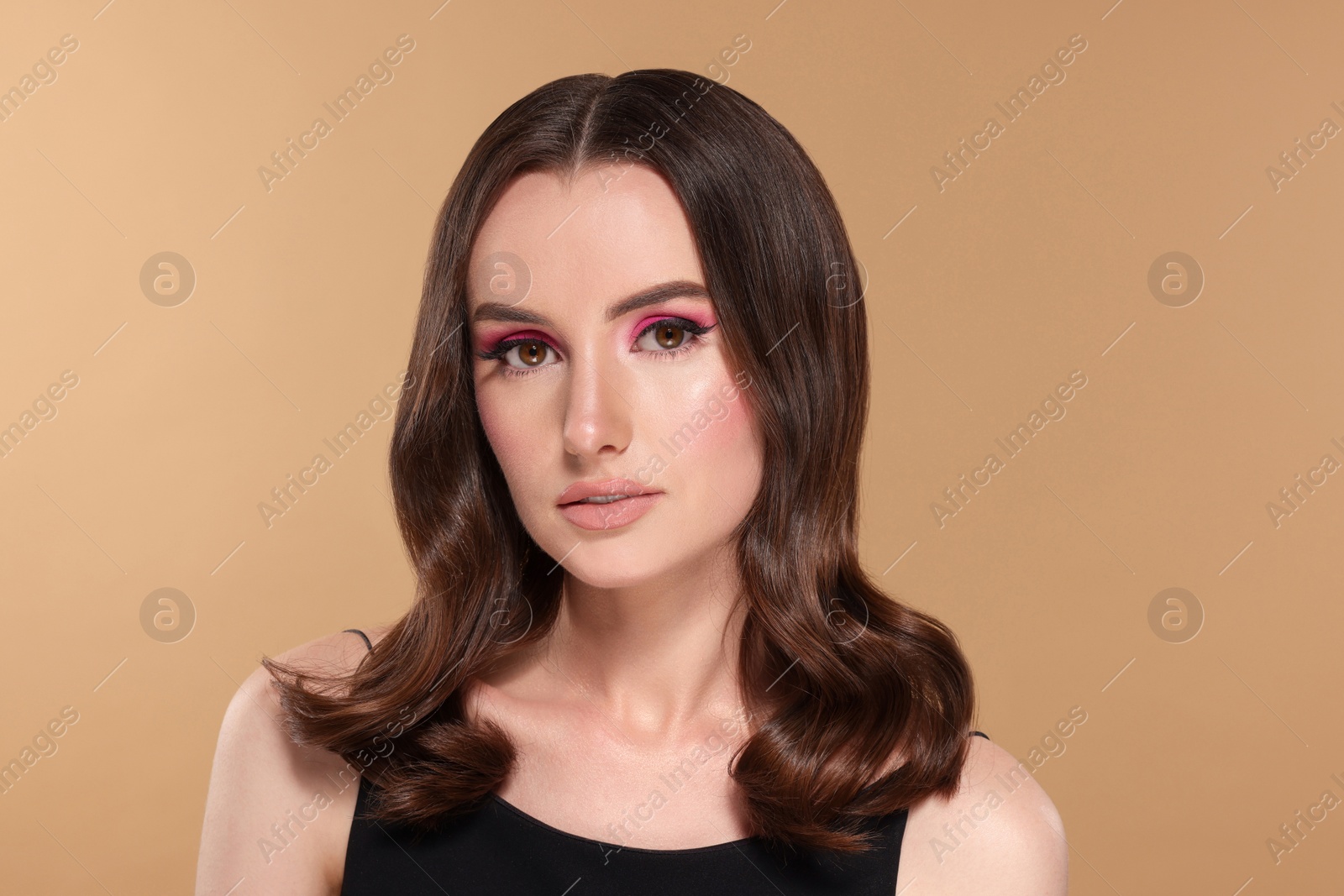 Photo of Portrait of beautiful young woman with makeup and gorgeous hair styling on beige background