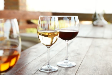 Photo of Glasses with different wines on wooden table in outdoor cafe
