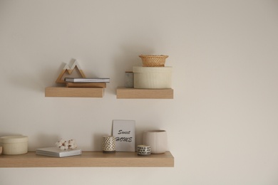 Wooden shelves with books and different decorative elements on light wall. Space for text