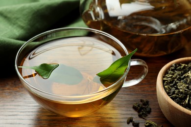 Photo of Fresh green tea in glass cup with leaves on wooden table, closeup