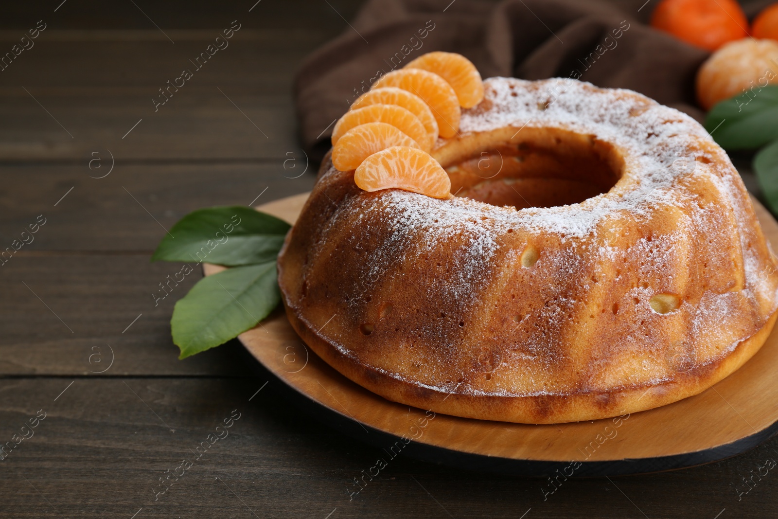 Photo of Homemade yogurt cake with tangerines, powdered sugar and green leaves on wooden table. Space for text