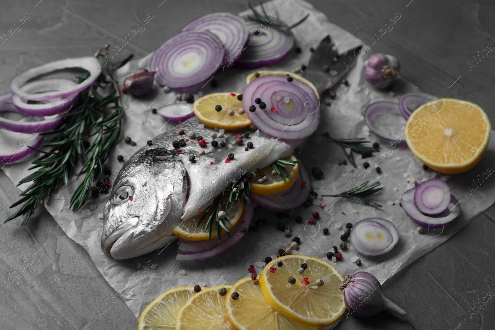 Photo of Raw dorado fish with spices, lemon and onion on grey table