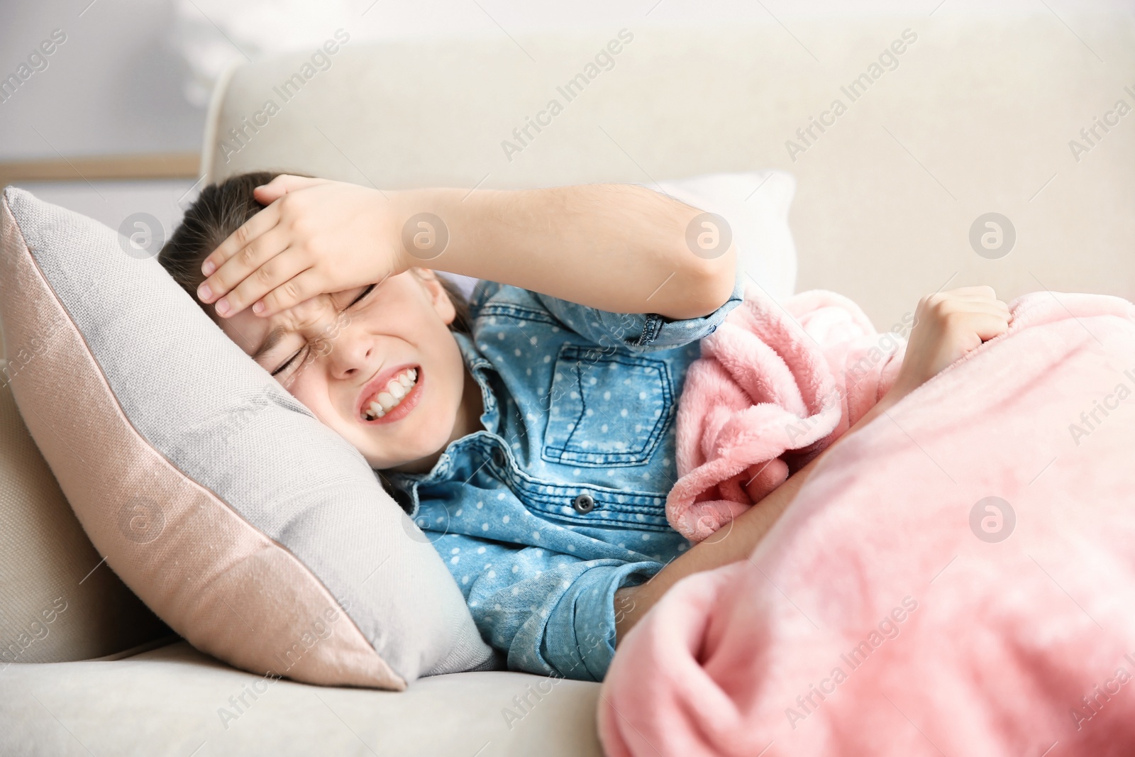 Photo of Little girl suffering from headache while lying on couch at home