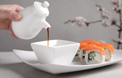 Woman pouring soy sauce for tasty sushi rolls at grey table, closeup