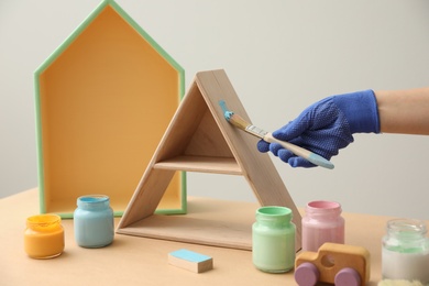 Decorator painting pyramid shaped shelf with brush at wooden table, closeup. Interior element