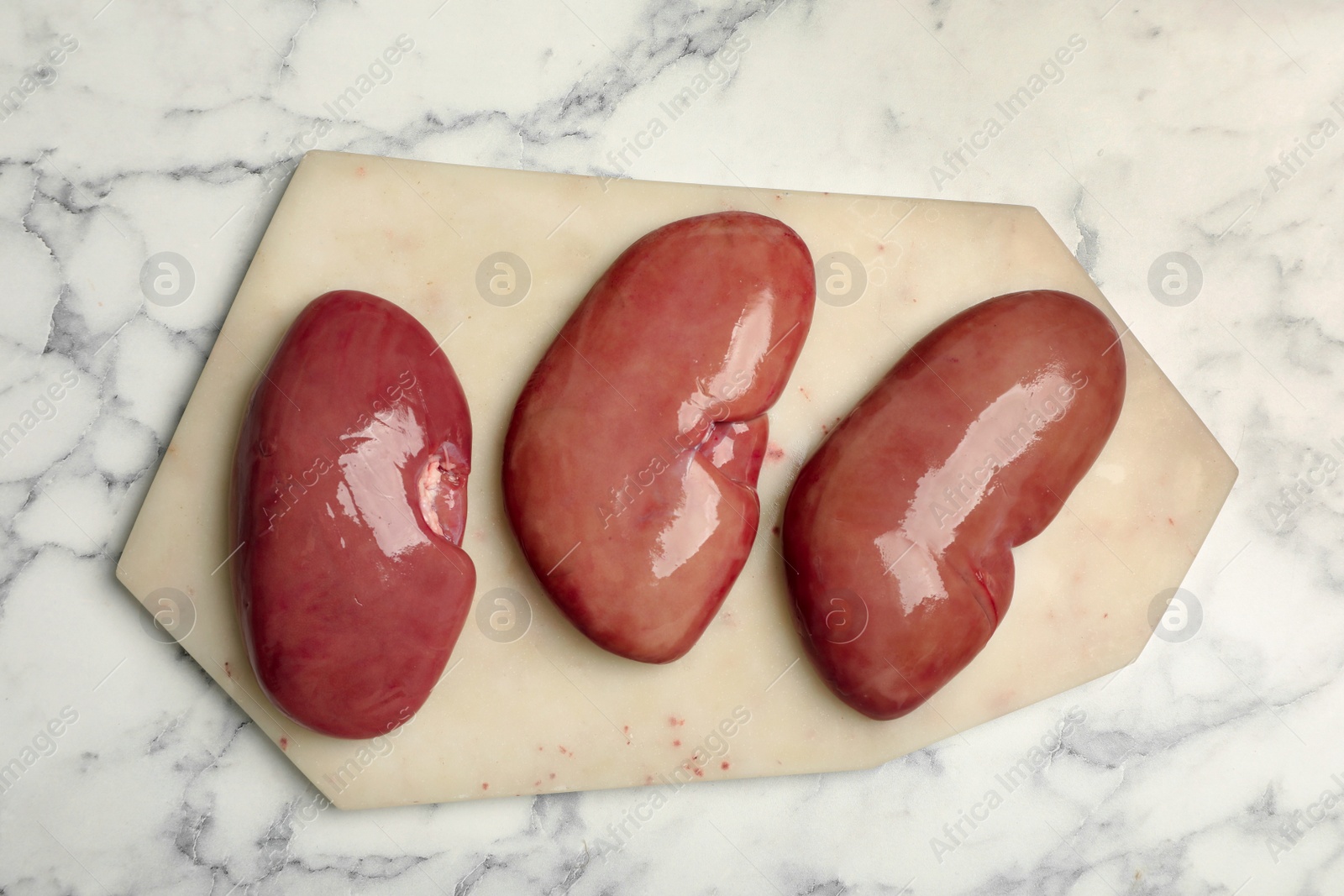 Photo of Fresh raw pork kidneys on white marble table, top view