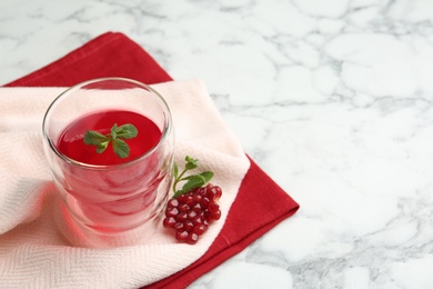 Photo of Glass of fruit jelly and pomegranate seeds on marble table, space for text