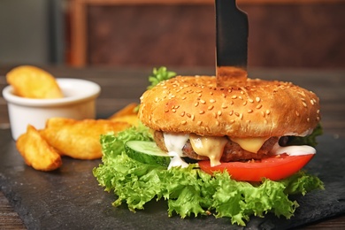 Photo of Tasty burger and fries served on slate plate, closeup
