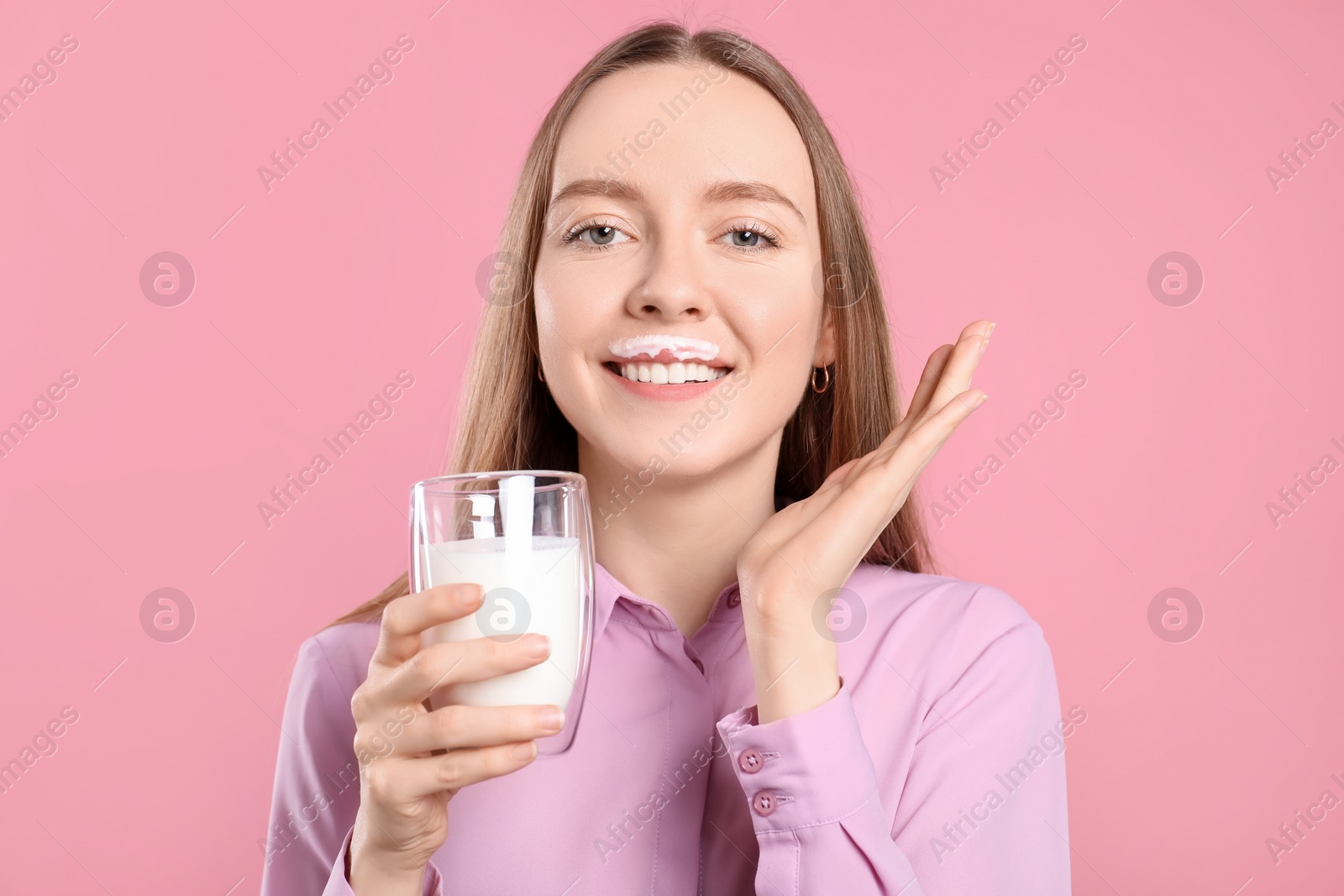 Photo of Smiling woman with milk mustache holding glass of tasty dairy drink on pink background