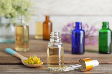 Photo of Bottle of essential oil, pipette and spoon with flowers on wooden table, space for text