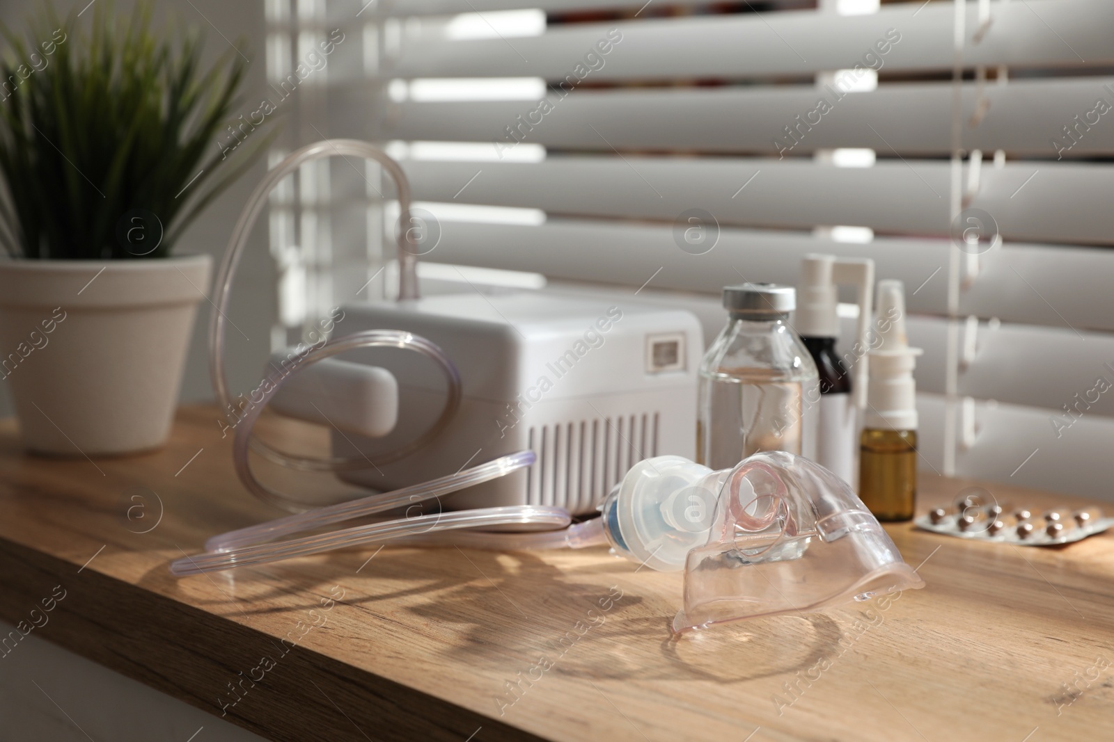 Photo of Modern nebulizer with face mask and medications on wooden table indoors. Inhalation equipment