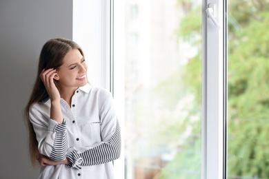 Young beautiful woman standing near window at home