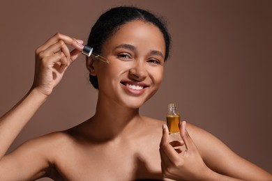 Smiling woman applying serum onto her face on brown background