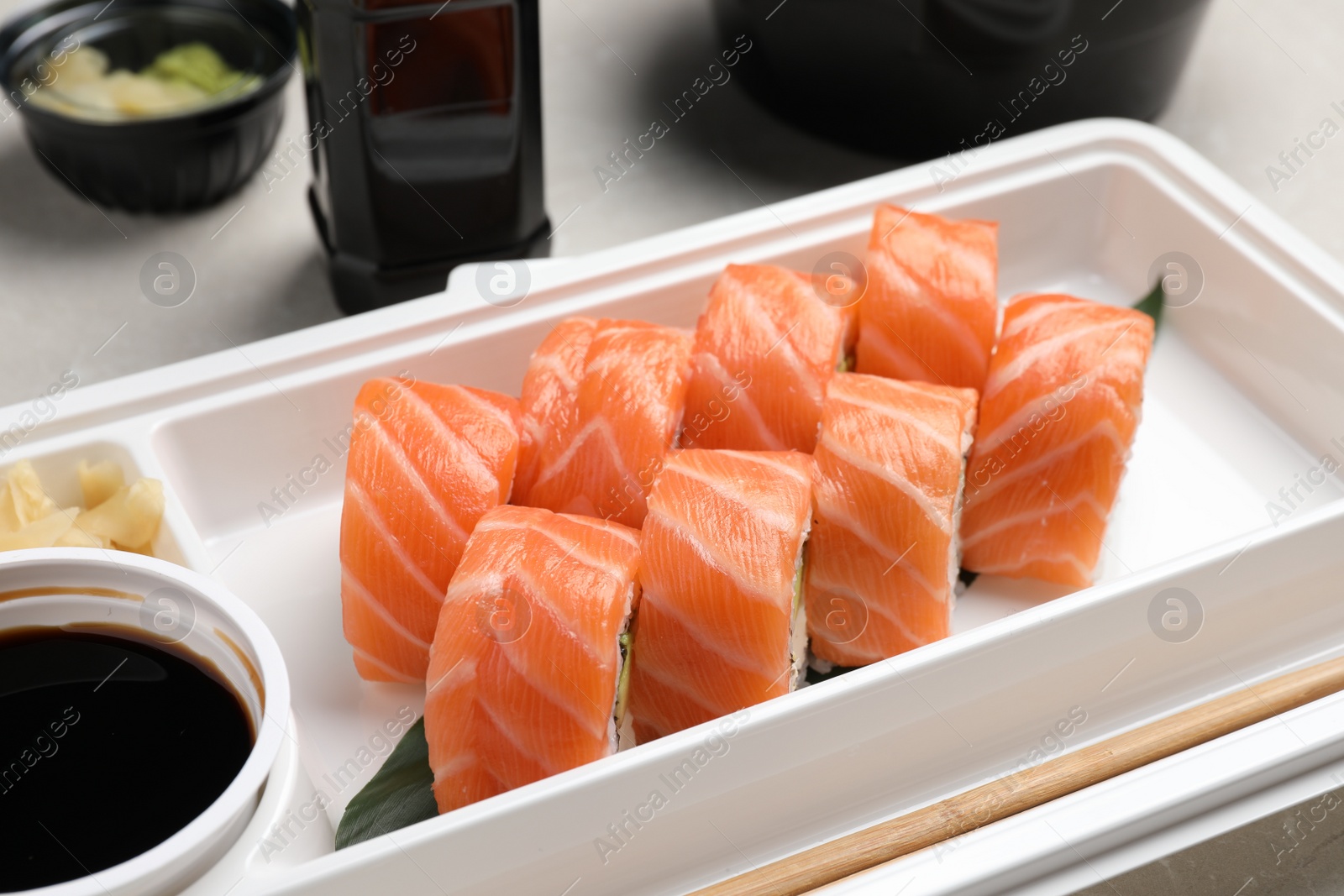 Photo of Delicious sushi rolls in plastic container, closeup. Food delivery