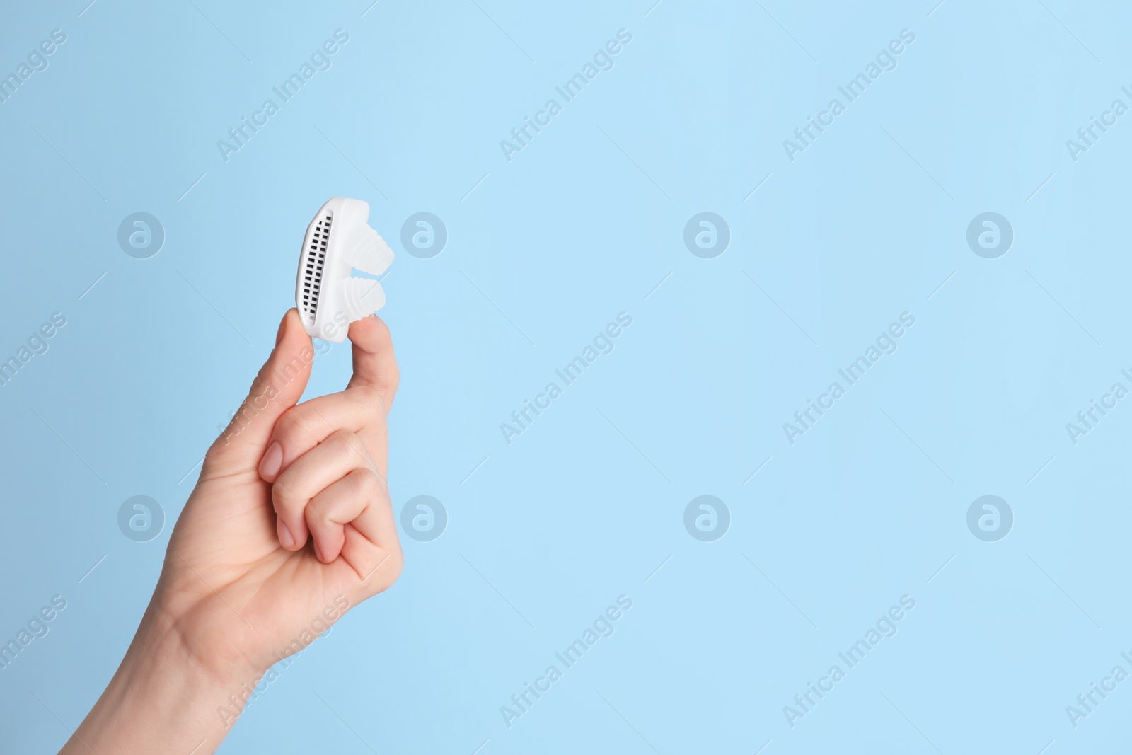 Photo of Woman holding anti-snoring device on light blue background, closeup. Space for text