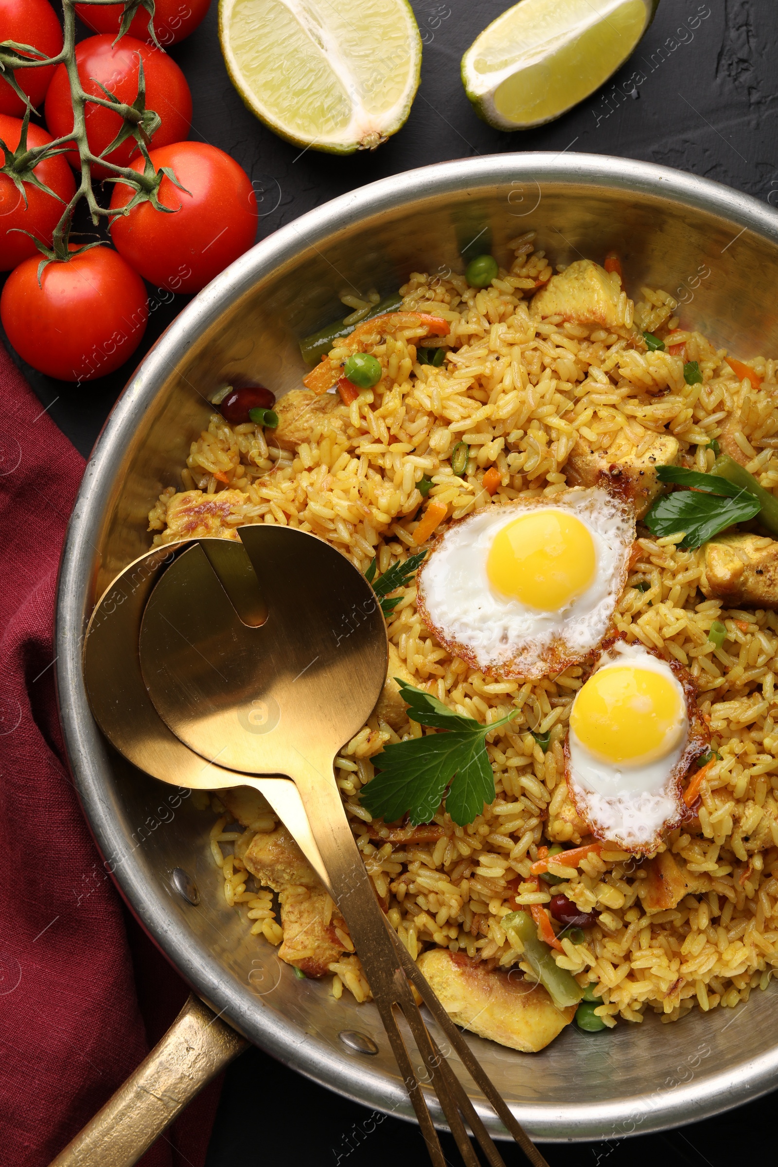 Photo of Tasty rice with meat, eggs and vegetables in frying pan near products on black textured table, flat lay