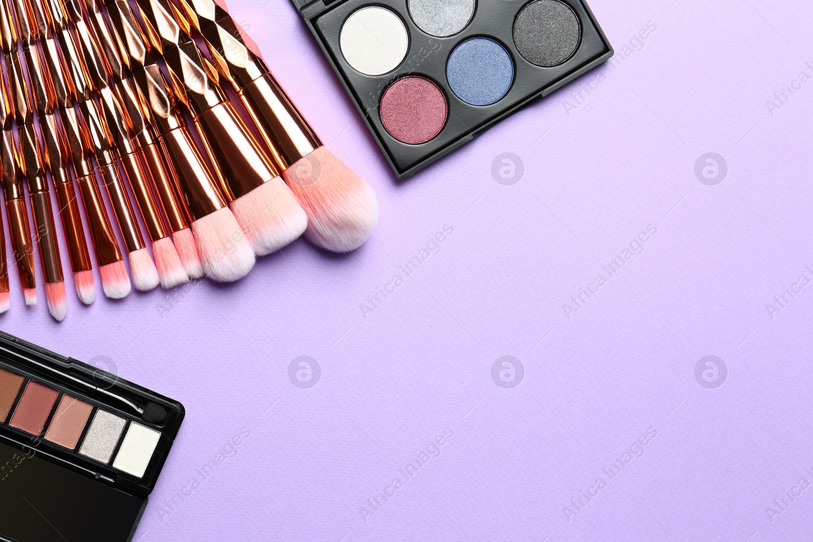 Photo of Flat lay composition with professional makeup brushes and eyeshadow palettes on lilac background. Space for text