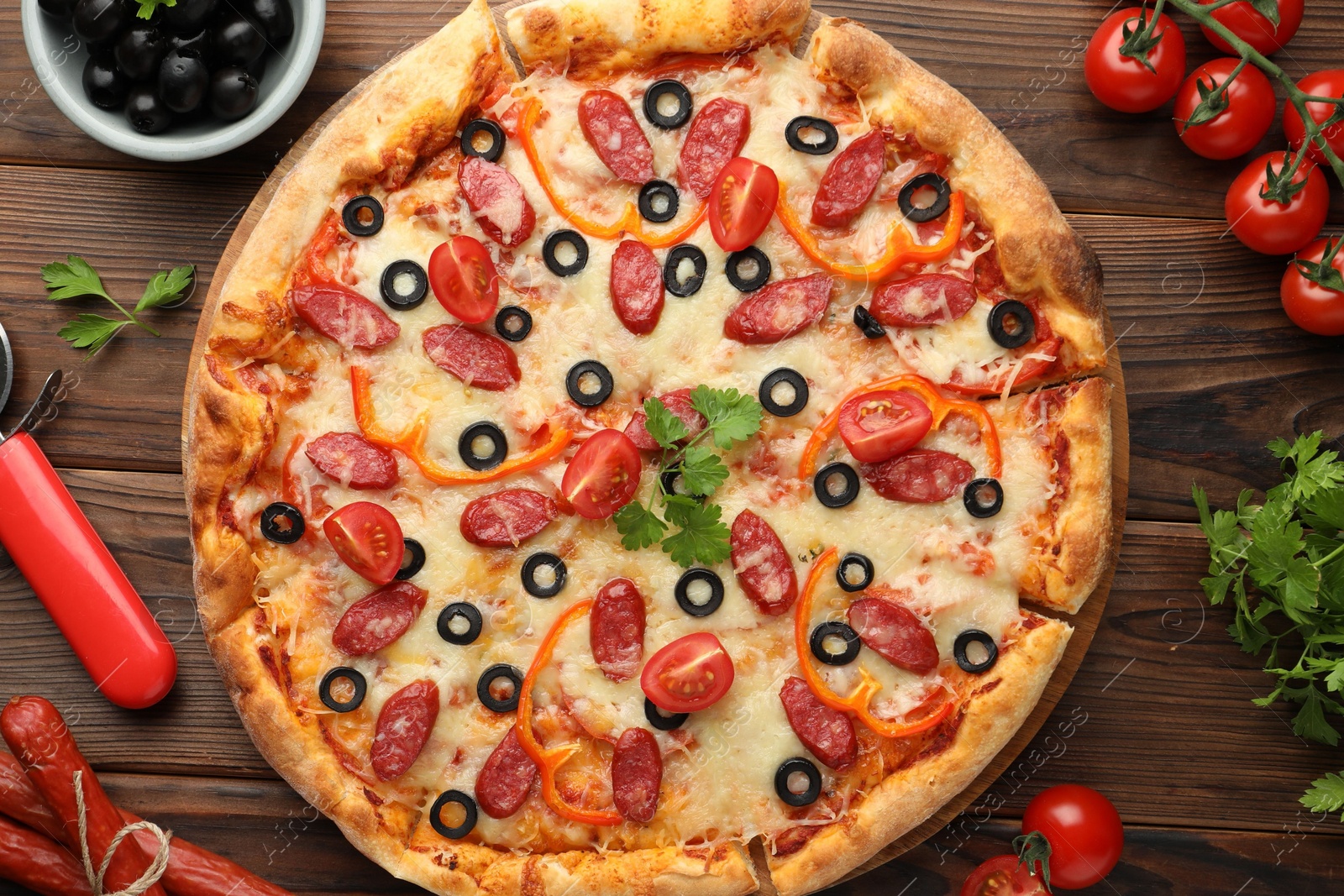 Photo of Tasty pizza, ingredients and cutter on wooden table, top view