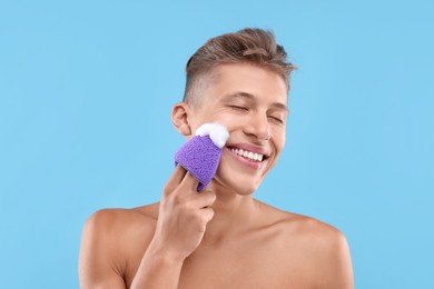 Photo of Happy young man washing his face with sponge on light blue background