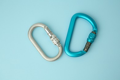 Photo of Two metal carabiners on light blue background, flat lay