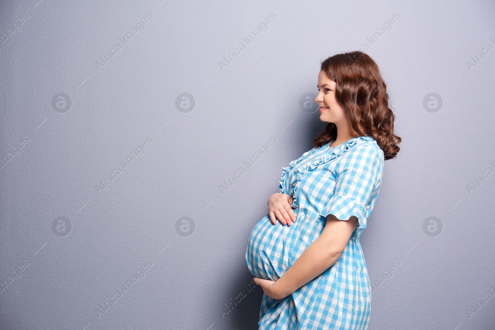 Photo of Young pregnant woman in casual clothes on grey background