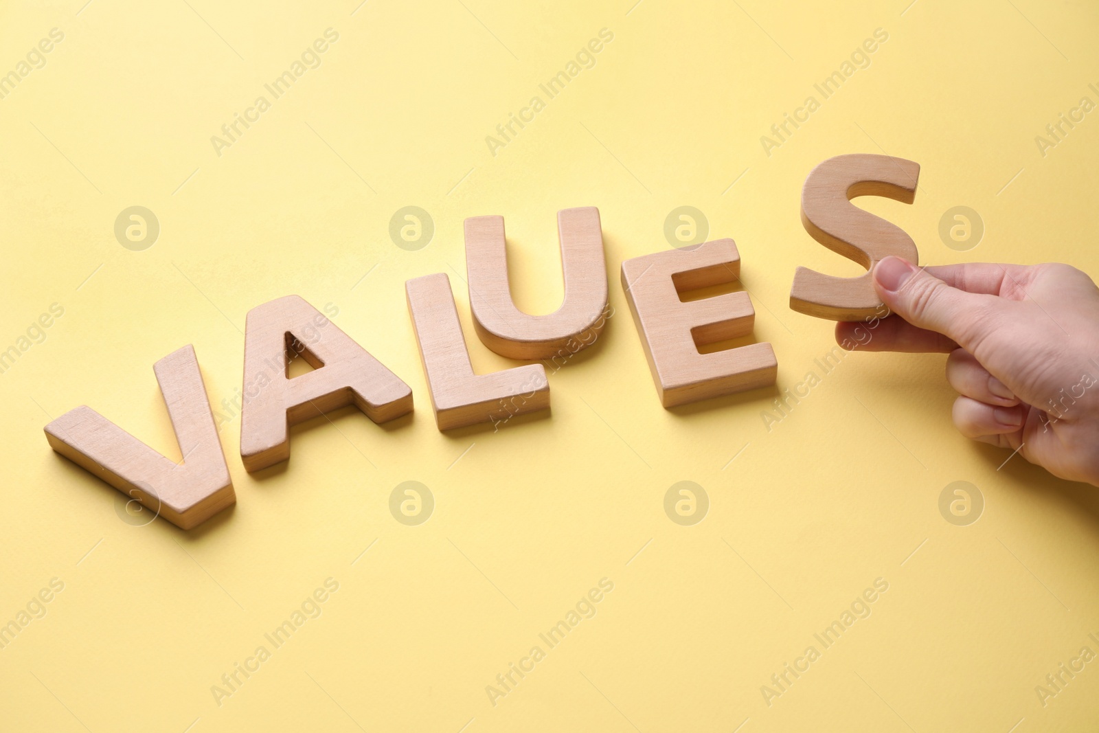 Photo of Woman making word VALUES with wooden letters on yellow background, closeup