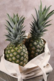 Photo of Bag with delicious ripe pineapples on table against pink wall, closeup